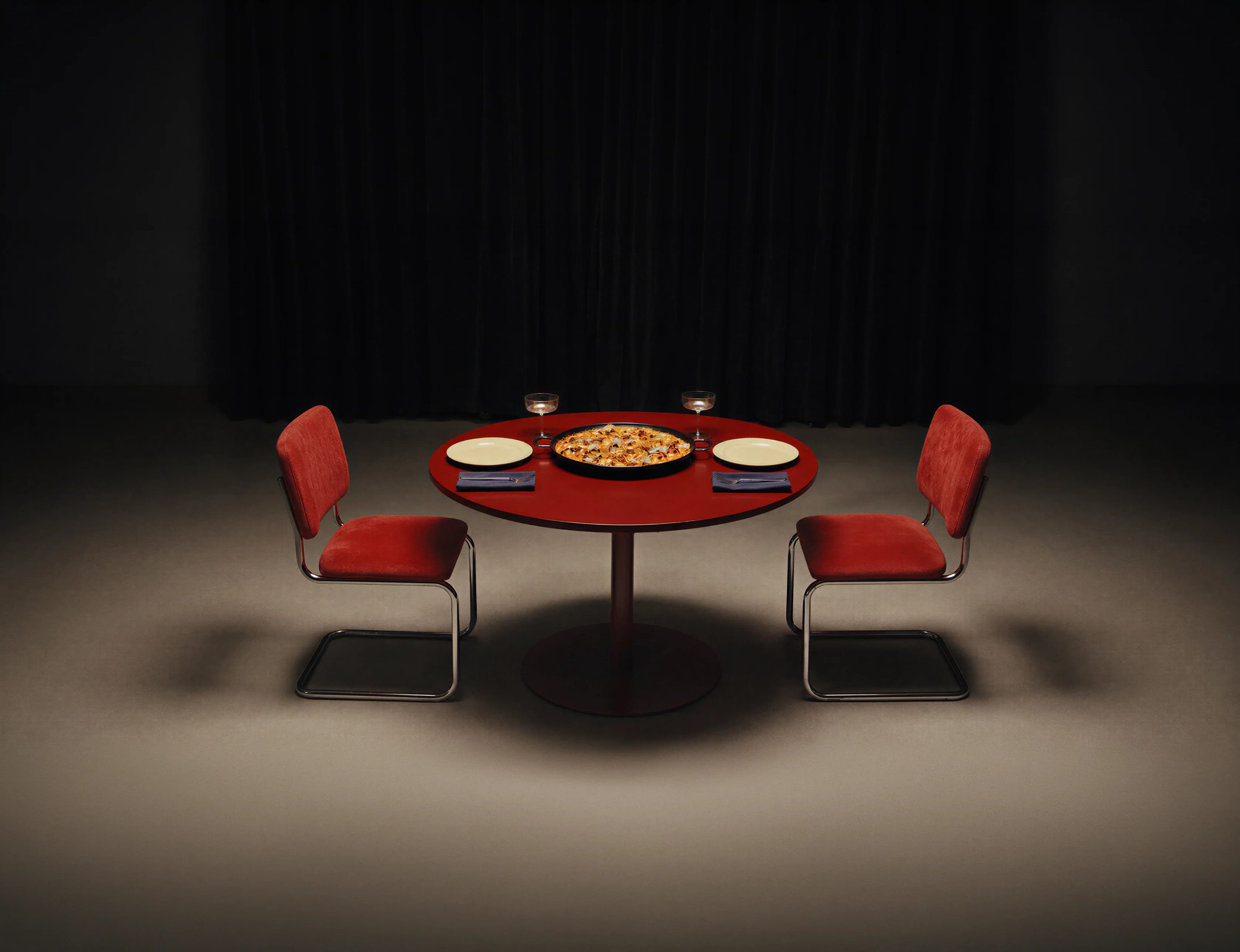 Mesa con una paella servida entre dos sillas rojas